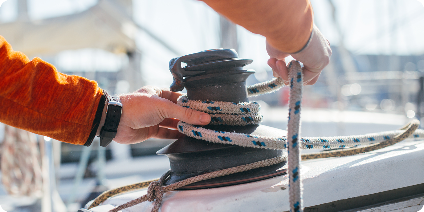 A sailor works with a winch and rigging on the deck of a yacht, demonstrating professional skills in maritime affairs